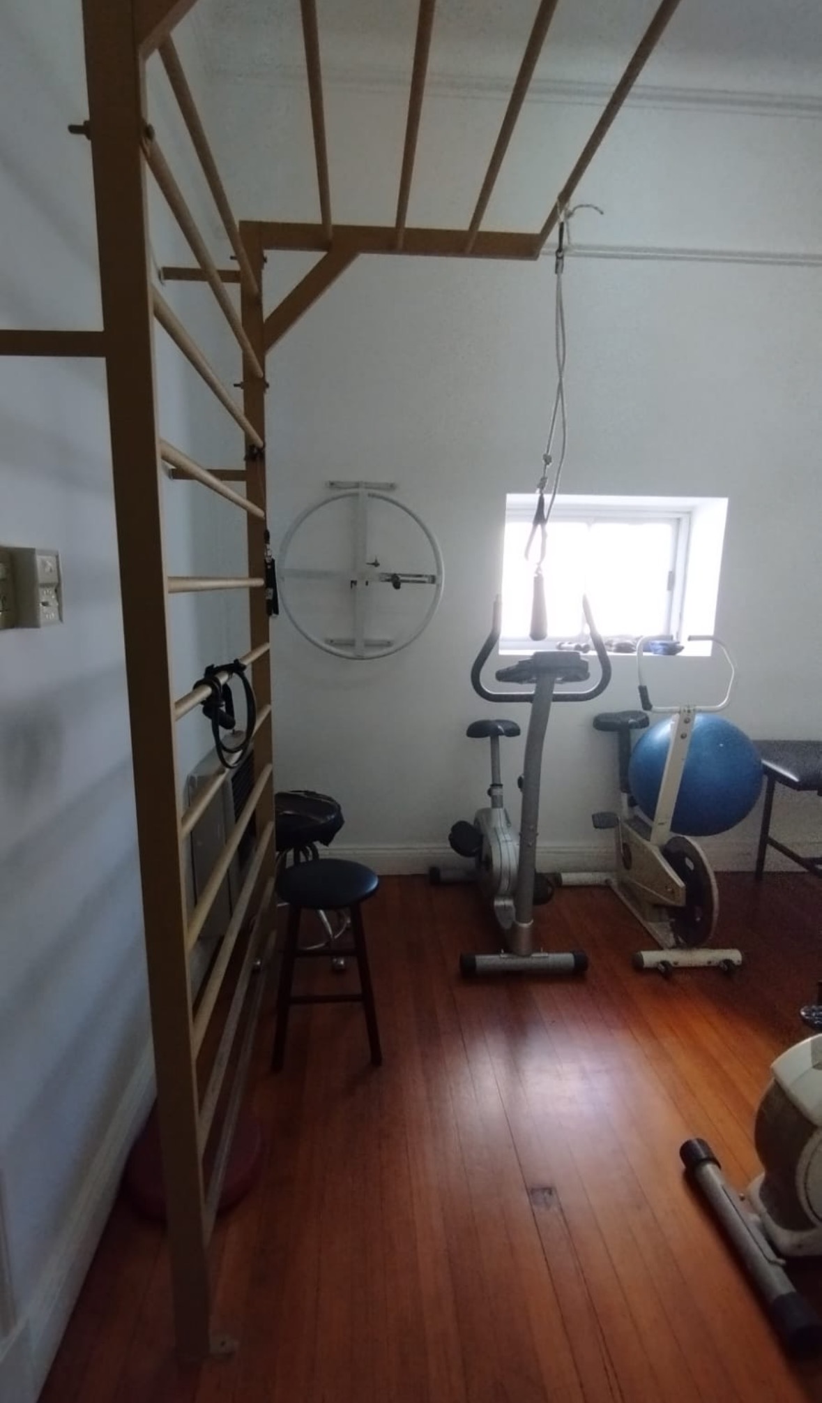 Sala de rehabilitación kinesiológica a domicilio, con espaldera, bicicleta fija y pelota de pilates